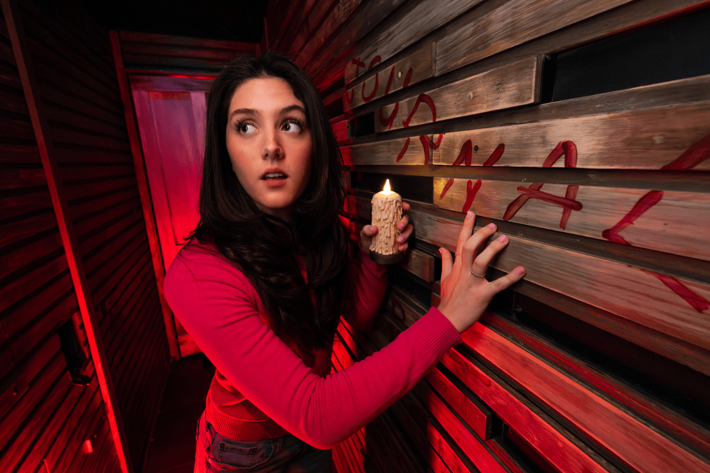 brunette girl holding a candle in a wood paneled hallway with an eerie red light